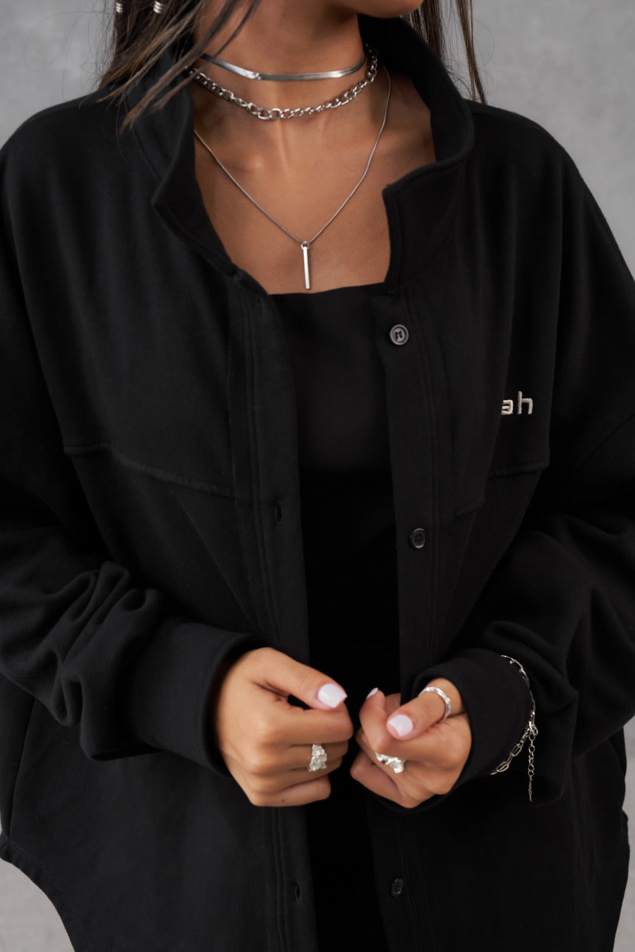 Black oversized French Terry overshirt with button detailing, paired with a black top and layered necklaces.