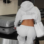 Person in a gray hoodie and matching grey sweatpants at an airport baggage claim area