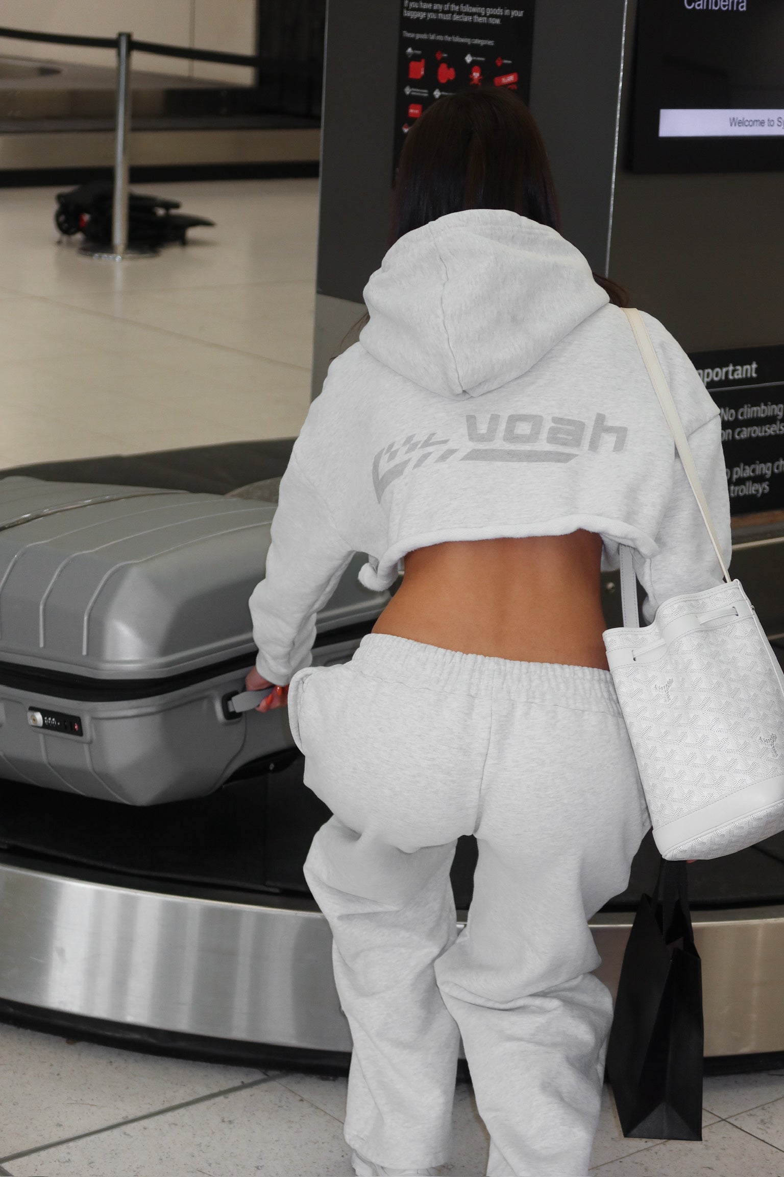 Person in a gray hoodie and matching grey sweatpants at an airport baggage claim area