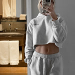 Person taking a mirror selfie wearing a gray hoodie and pants in a bathroom.