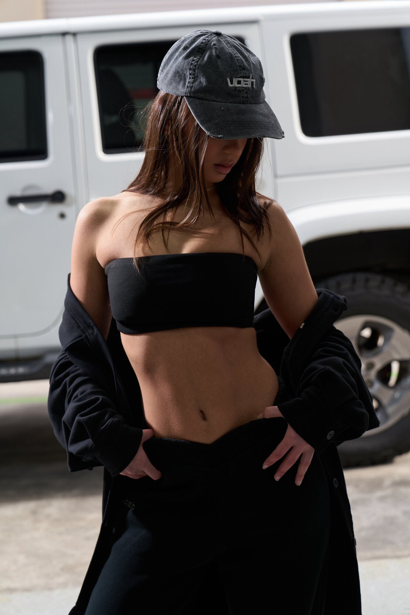 model wearing a black strapless top and cap in front of a white jeep.